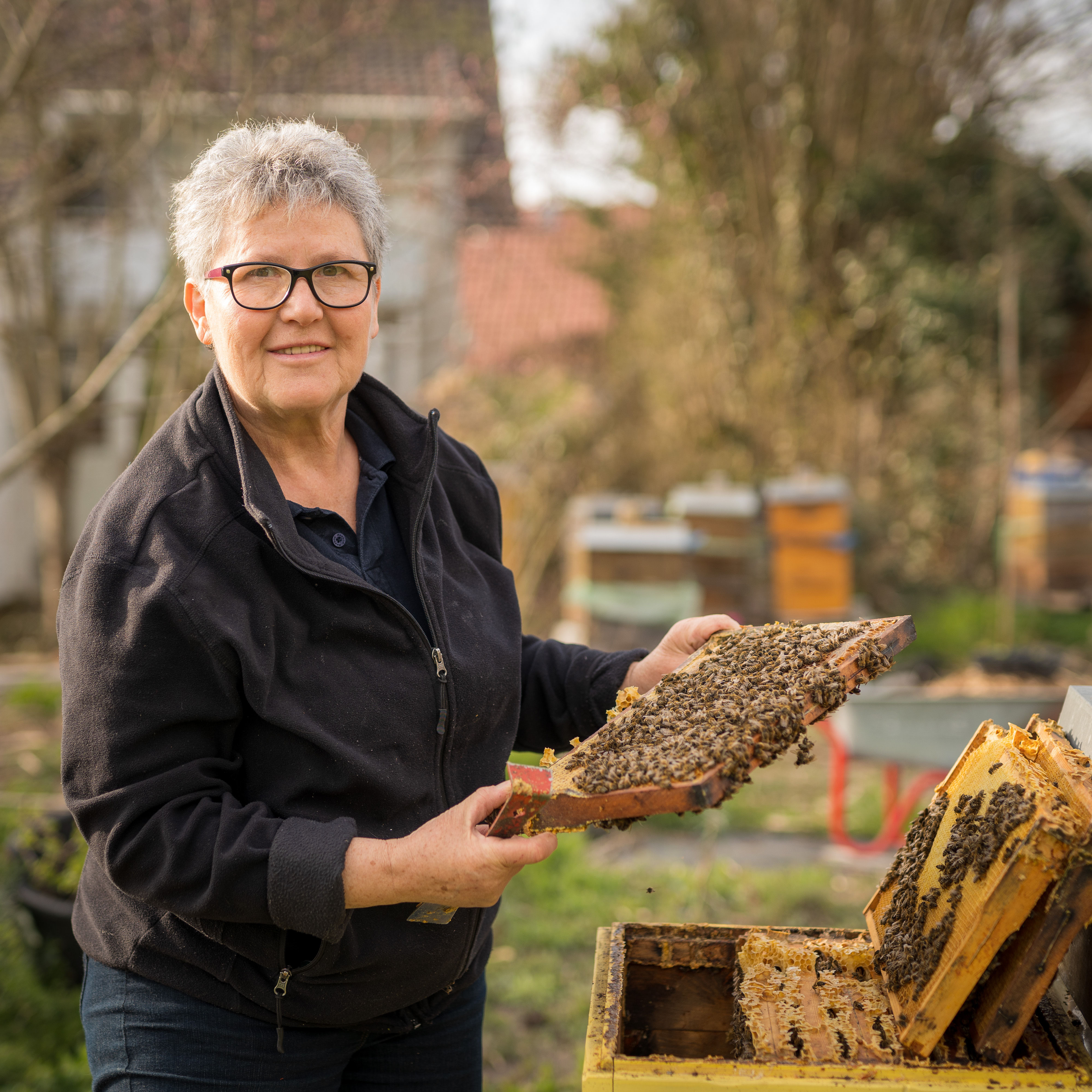 Porträtfoto von Christa Wohriska im Freien, sie hält eine Bienenwabe in den Händen
