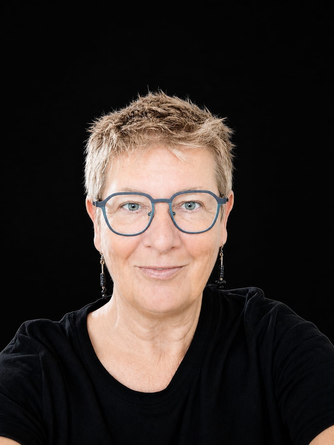 Porträtfoto von Doris Wimmer vor schwarzem Hintergrund, kurze graue Haare und Brille