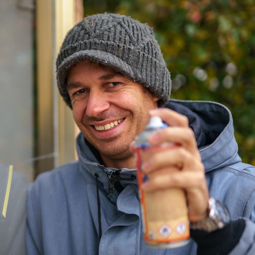 Porträtfoto von Felix Baumann mit Wollmütze, er lächelt und hält eine Sprühdose in der Hand