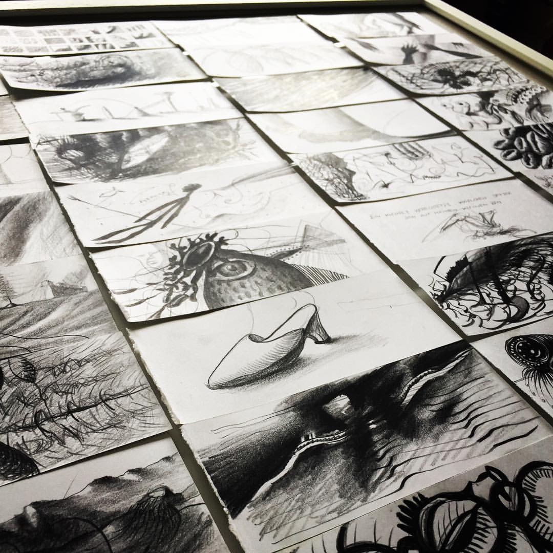 Fotografie eines Tisches mit vielen ausgebreiteten Bleistift- und Kohleskizzen, darunter ein Schuh und ein Fischkopf