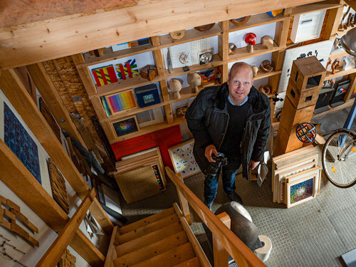 Rainer Menkhaus mit Kamera in der Hand, von oben fotografiert in einem mit Kunst und Fotoarbeiten eingerichteten Atelier