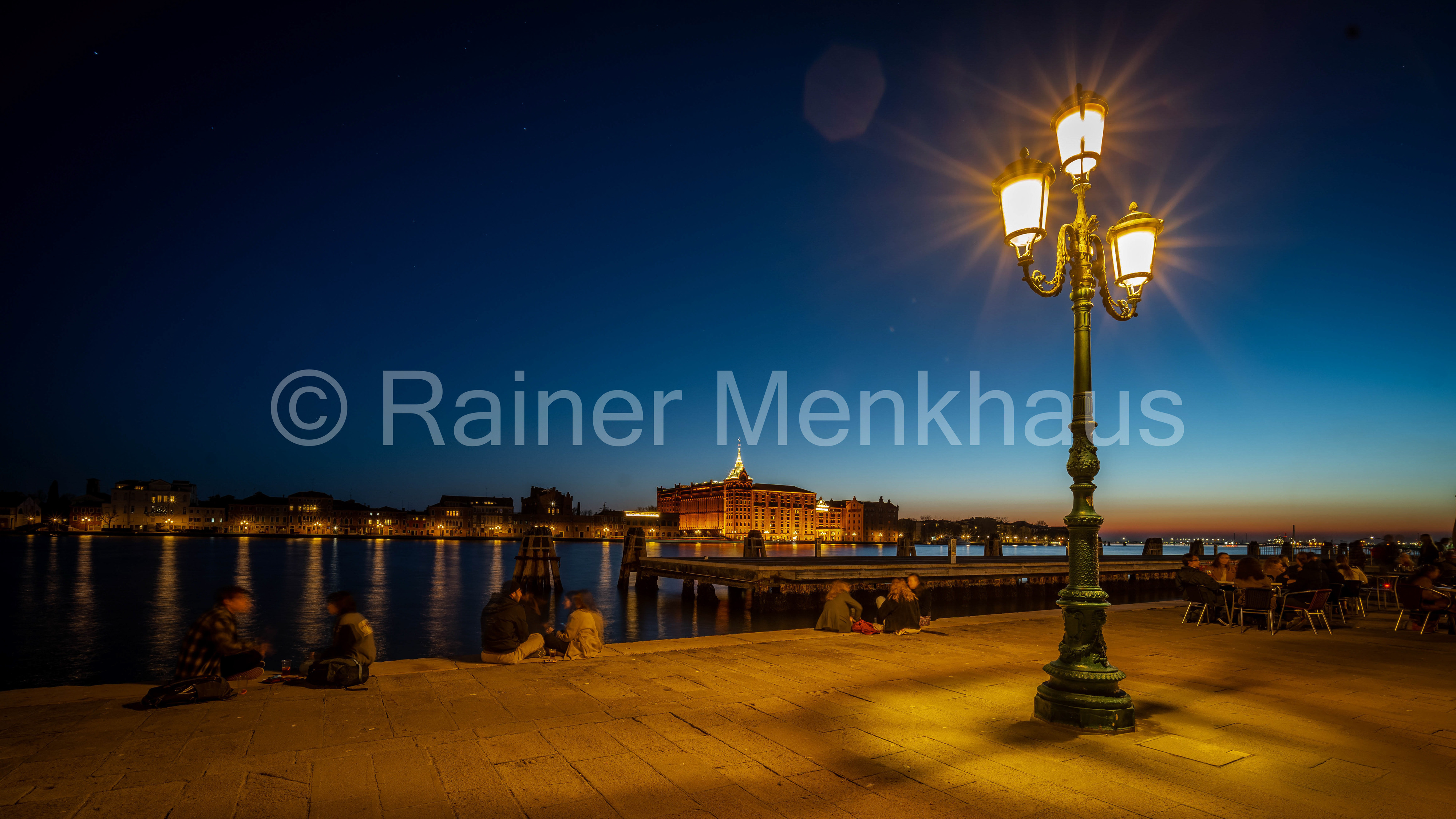 Beleuchtete Straßenlaterne an einer Uferpromenade in der Abenddämmerung