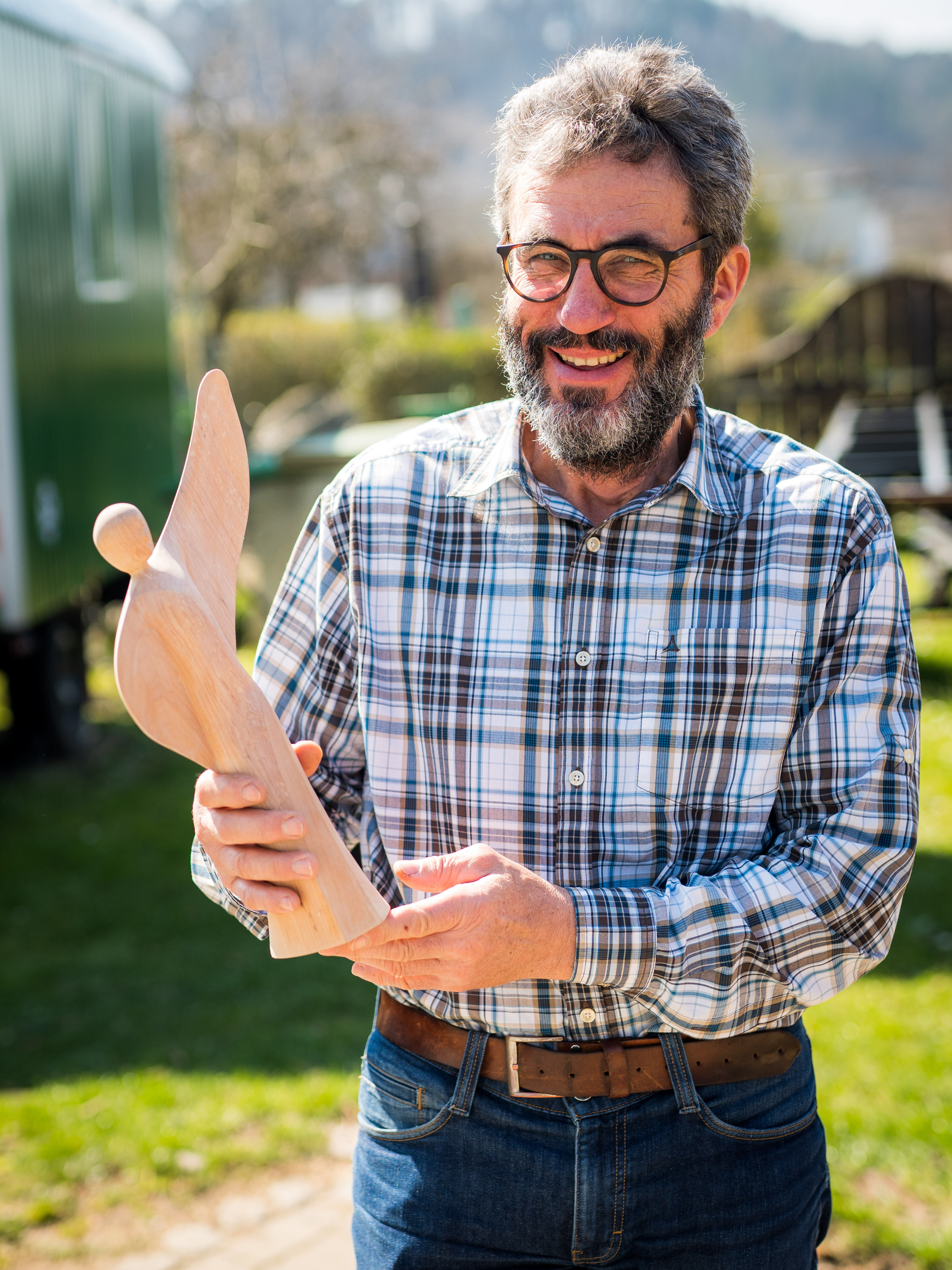 Thomas Schönenberger im Freien, hält eine geschnitzte Holzfigur in Vogel- oder Engelform in den Händen