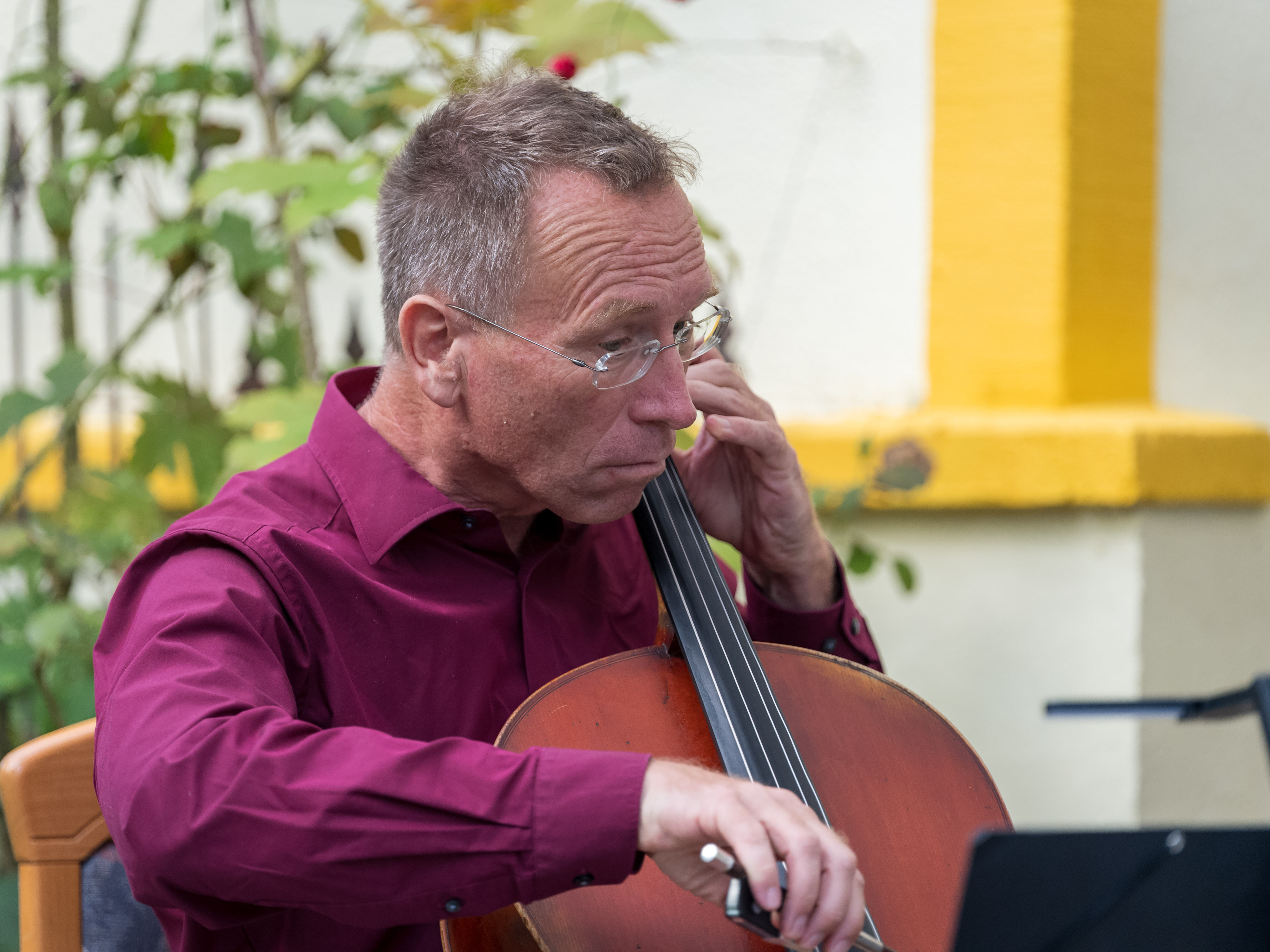 Ein Cellist spielt vor einer weiß-gelben Hauswand