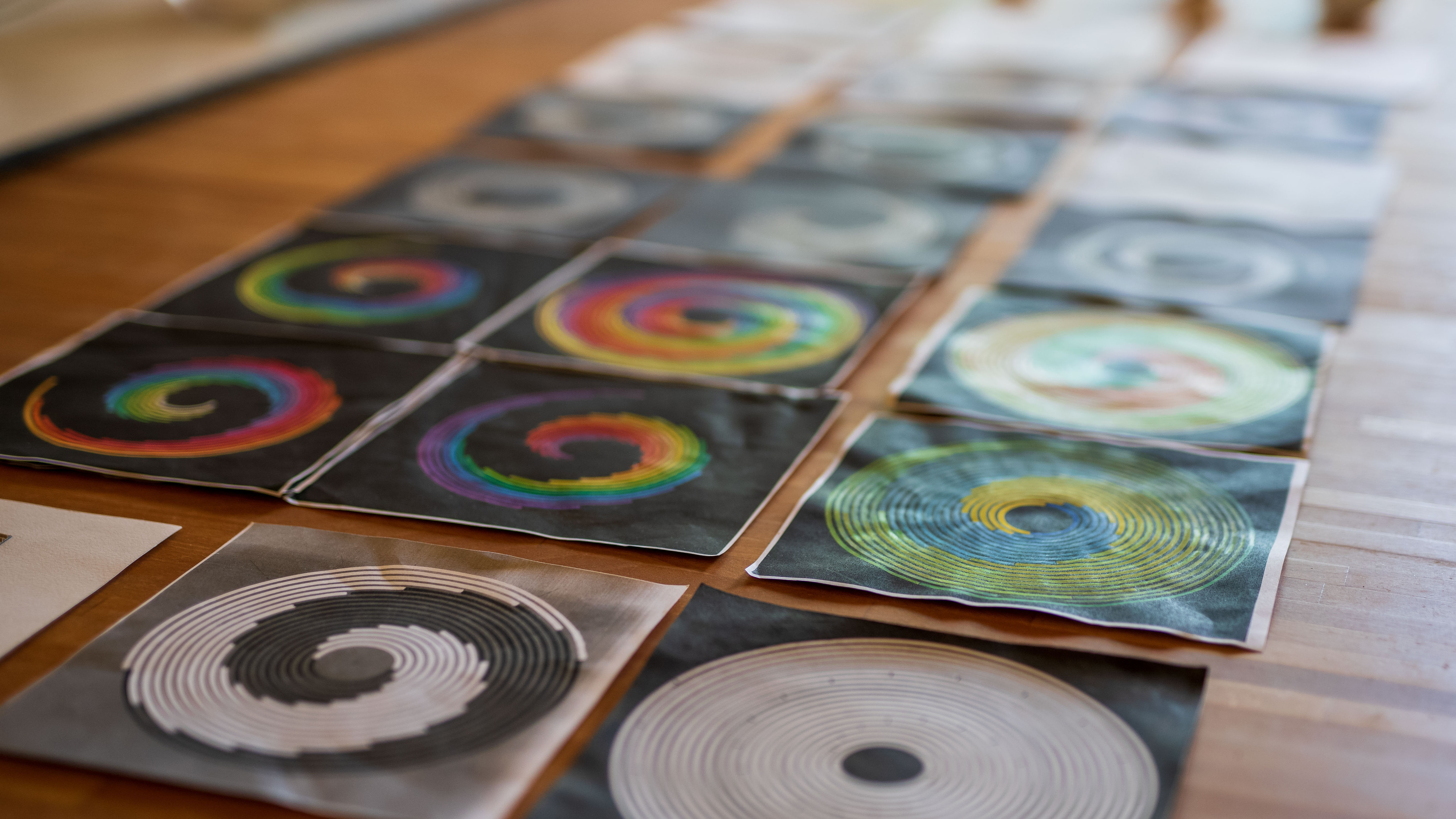 Sechs runde, bunte Spiralbilder in verschiedenen Farbkombinationen auf einem Holztisch ausgelegt