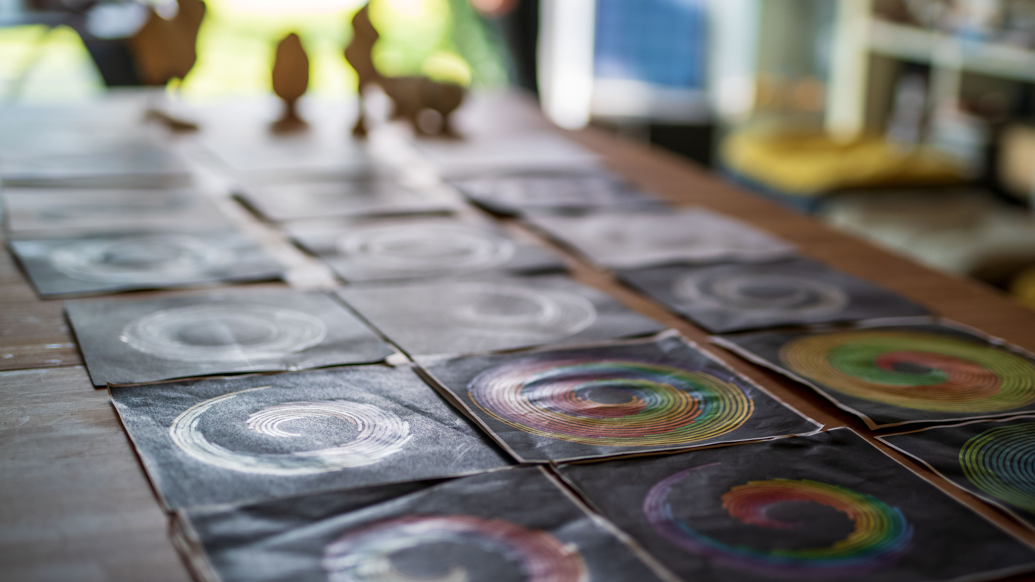 Weitere runde Spiralbilder auf einem Tisch, im Hintergrund kleine Holzfiguren