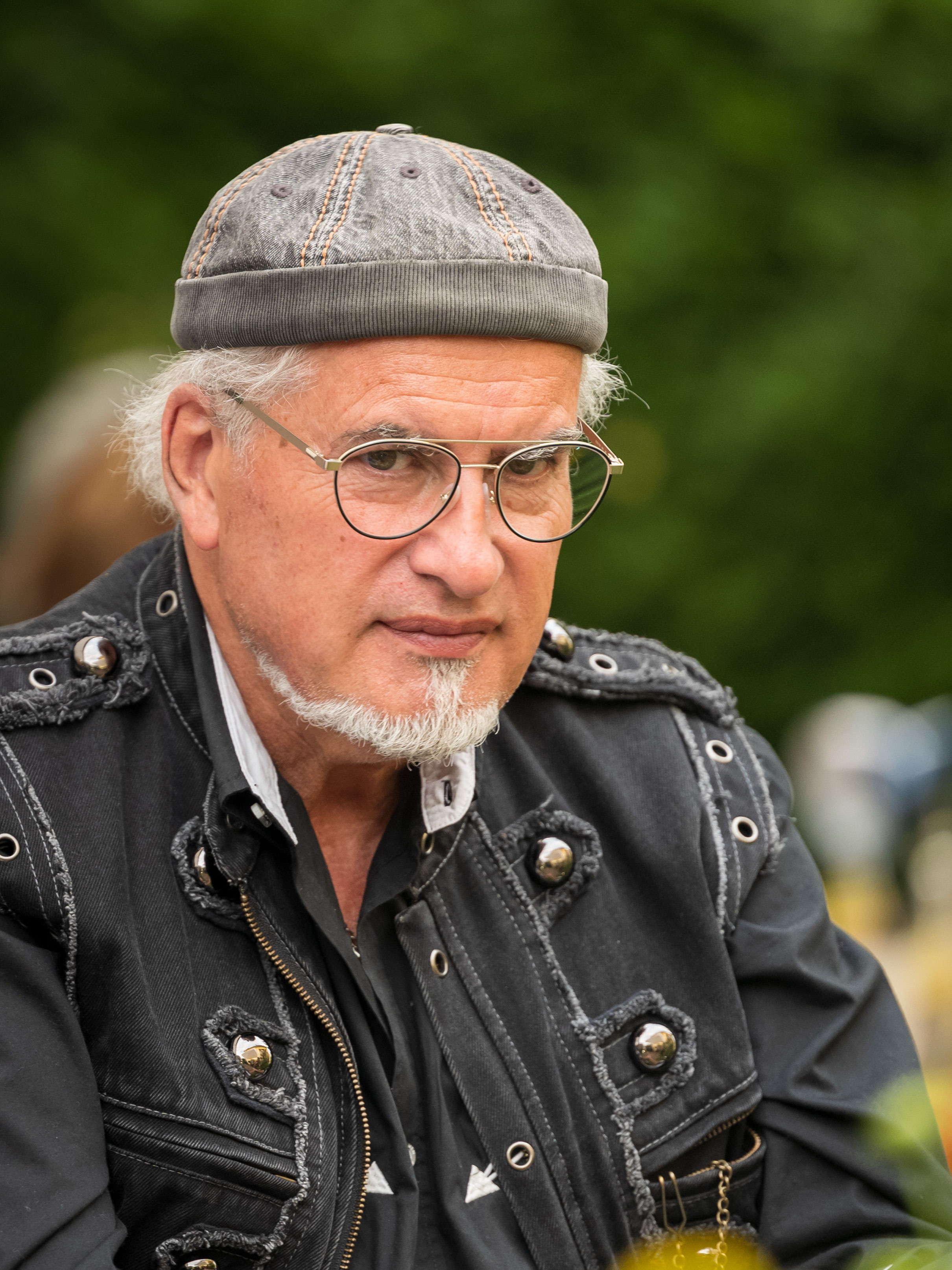 Porträt eines Mannes mit Schirmmütze und Brille vor grünem Hintergrund