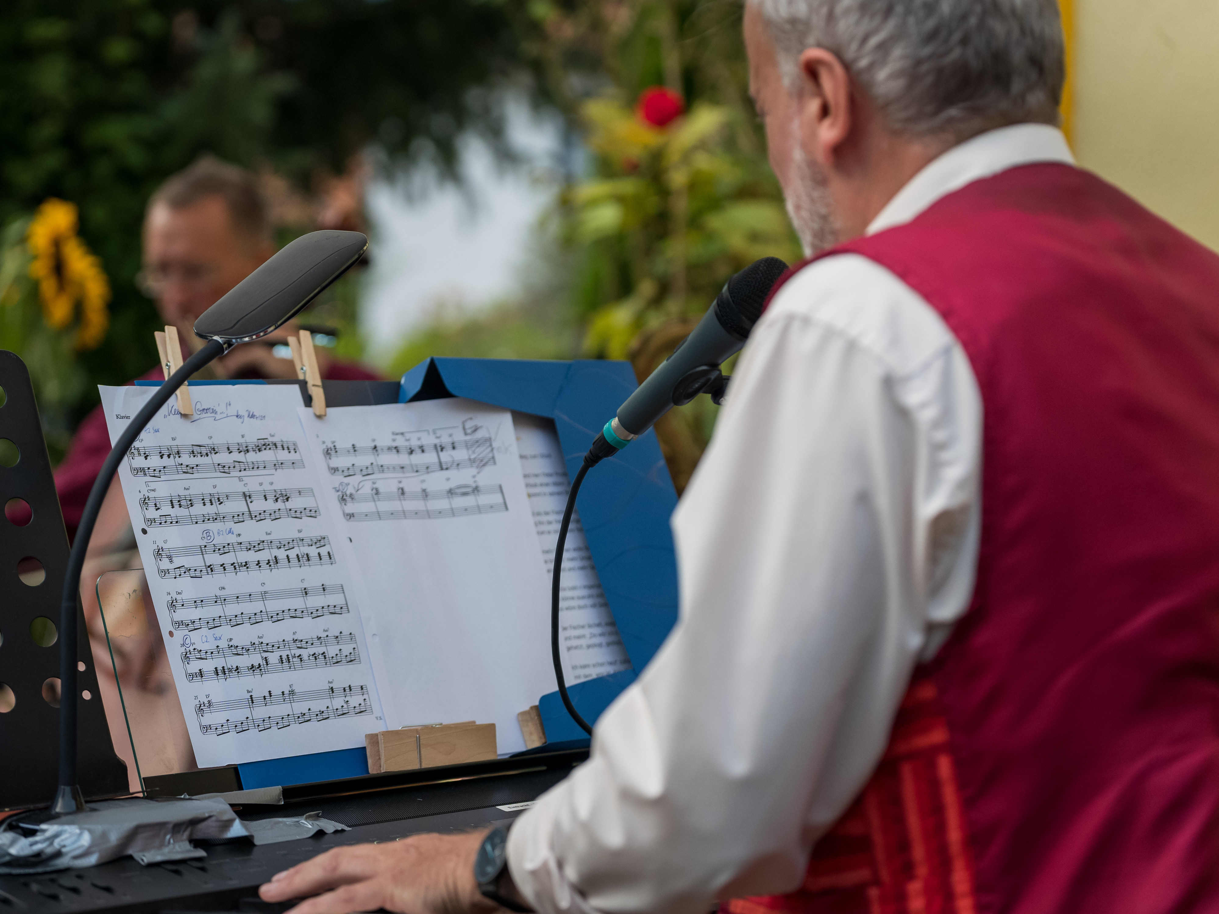 Ein Mann in roter Weste singt an einem Notenständer mit Mikrofon