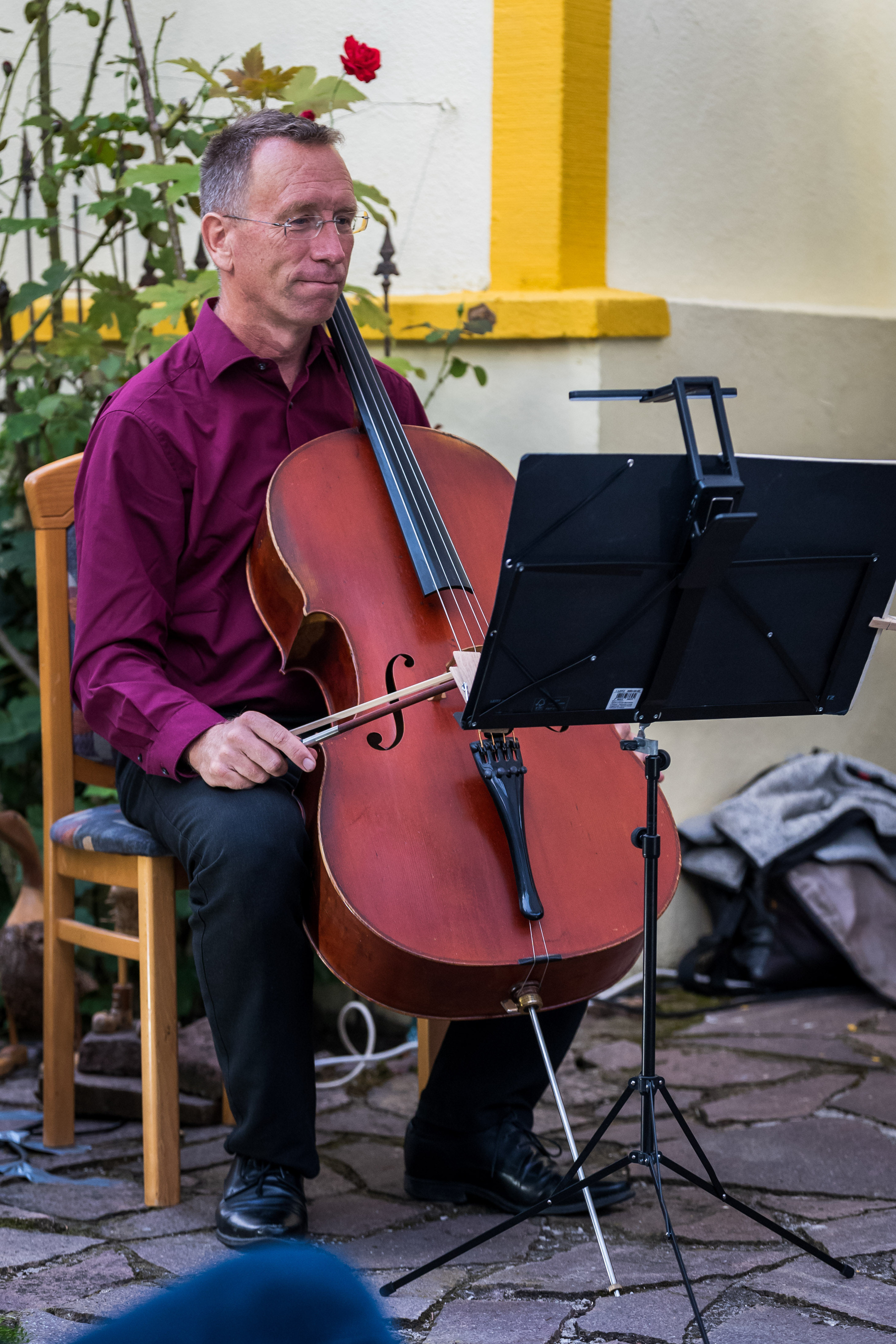 Ein Mann spielt Cello vor einem Notenständer auf einer Terrasse