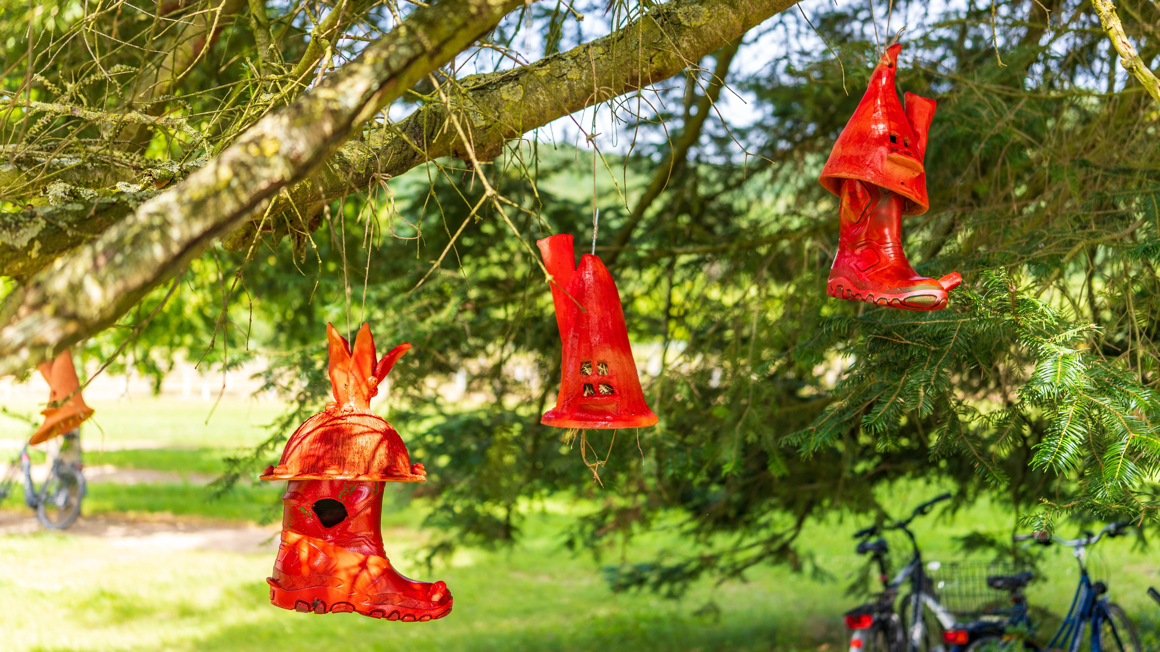 Rote, figürliche Kunststoffobjekte hängen an Ästen eines Baumes