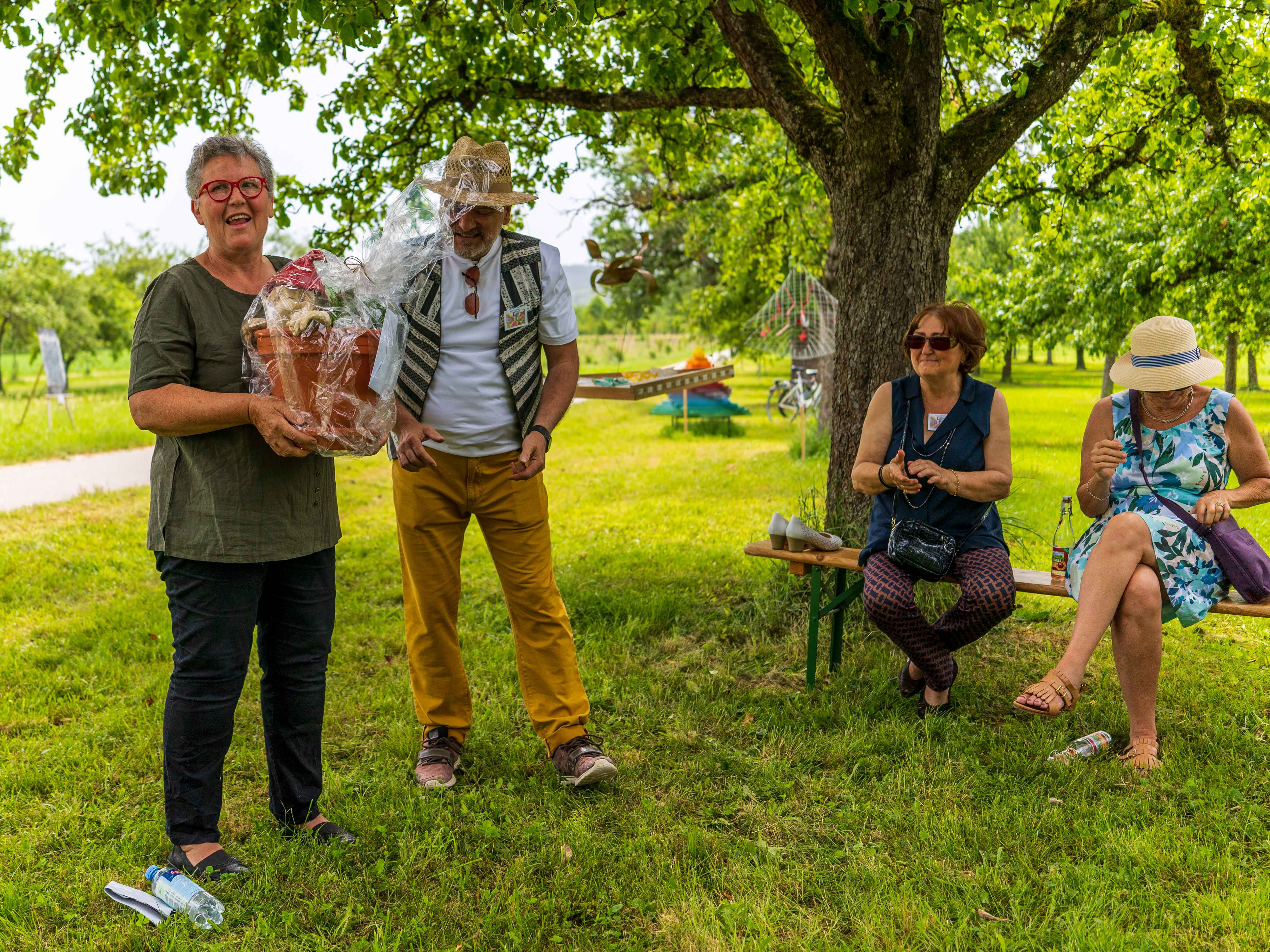 Zwei Männer und zwei Frauen unter einem Baum, einer der Männer hält einen Geschenkkorb in den Händen